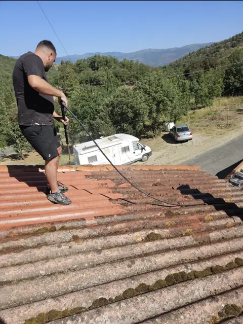 Joffrey, couvreur d’ASJ Toiture, nettoie une toiture en tuiles face aux collines
